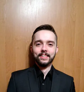 Adrian Gajdzik wearing a black suit in front of a wooden panel