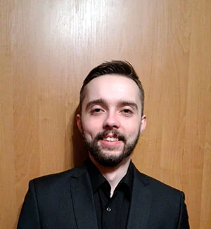 Adrian Gajdzik wearing a black suit in front of a wooden panel