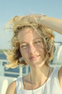 Ida Kajsa looking to towards the camera and holding her hair on a windy day by the sea