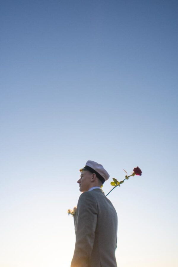 An artistic perspective of a man holding a long-stemmed rose on his shoulder.