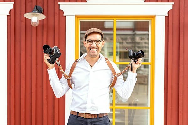 Aarón holding two cameras with a big smile on a red wooden background