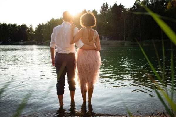 A wedding couple standing with their feet in the sea, gazing towards the sunset.