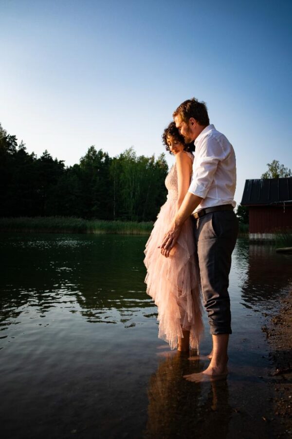 A wedding couple standing with their feet in the sea, striking a romantic pose.