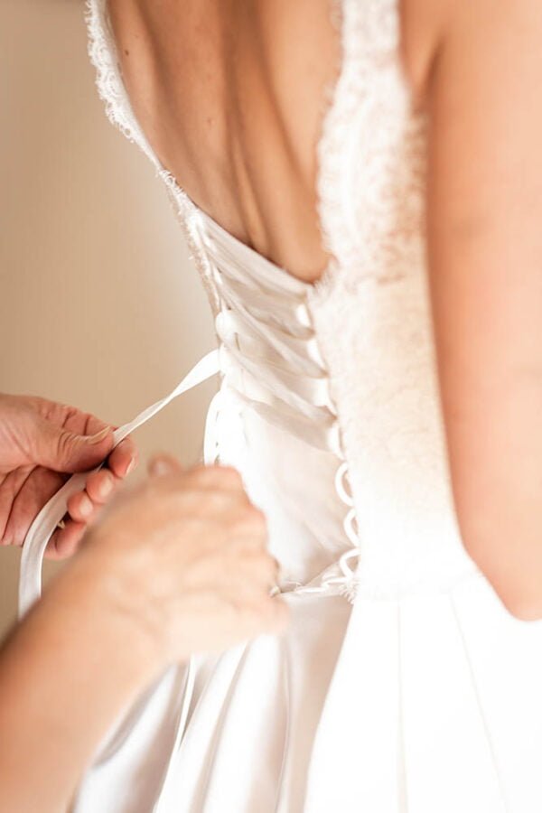 The mother is tying the lace of the bride’s wedding dress.