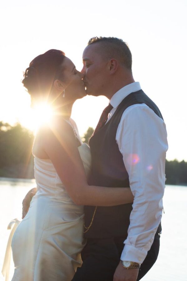 A wedding couple kissing each other in front of the sea with an incredible sunflare.