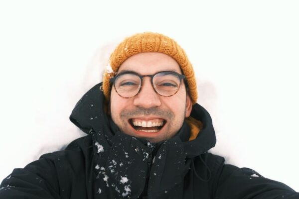 Aarón, with an orange hat, is lying on the snow with a big smile on his face.